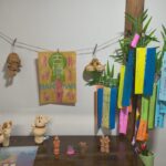 Clay figurines displayed on a wooden surface with a string of colorful Tanabata wish-tags in the background.