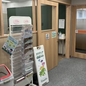 Reception area with wooden counters and a clear brochure rack filled with pamphlets and posters in Japanese.